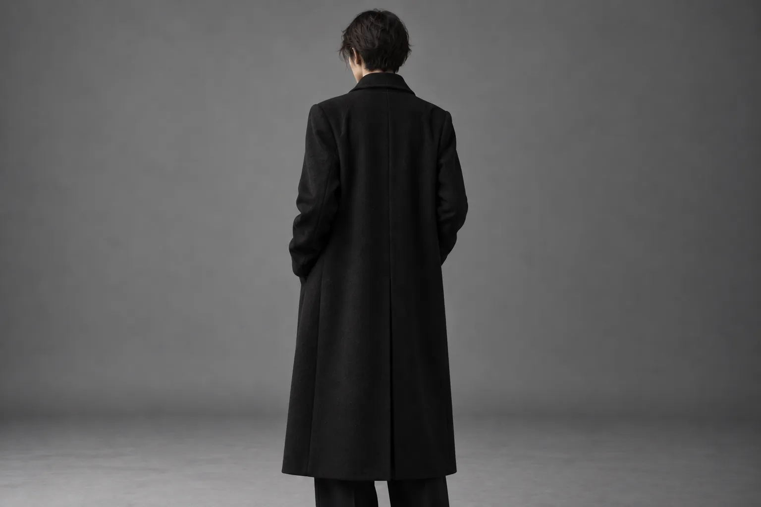 黒の長いコートを着た人物の後ろ姿。顔は背けている。(サンプル)